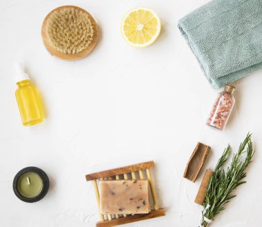 Organik cilt bakım ürünleri flatlay doğal sabun, petrol şişe, fırça, mum, tuz, havlu, biberiye bitki, limon ve tarçın, temiz minimalist gri beton arka plan kopya alanı ile