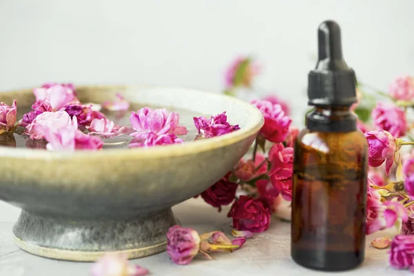 Ambiente de spa con rosas. Botella de aceite de rosa con cuenco de agua rosa para — Foto de Stock