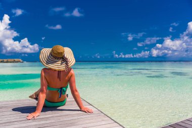 Bikini ve plaj ahşap iskelesi ve Lüks su villa yalan şapka güzel çekici kadın. Deniz manzaralı, lüks yaşam tarzı arka plan. Pastoral lüks konsepti. Bir plaj rahatlatıcı üzerinde güzel kadın
