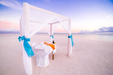 Gün batımında sahilde romantik bir akşam yemeği. Sahil manzaralı lüks bir tatil köyü, beyaz kum ve renkli gökyüzü. Idyllic balayı ve çift kaçamağı. 