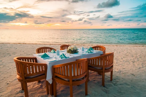 A romantic cozy family dinner in summer on a beach at sunset with wine glasses and napkins ready to eat. Serving for romantic dinner on a beach at summer sunset