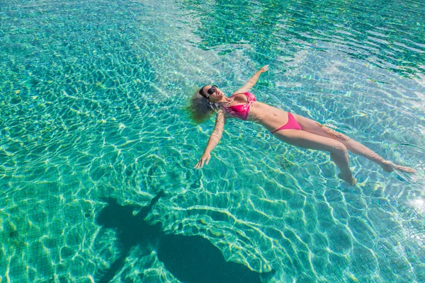 Young woman relaxing in swimming pool on summer vacation. Blonde caucasian model in red bikini floating in water. Young woman relaxing in the pool, luxury summer vacation, recreational travel. Peaceful, tranquility vibes