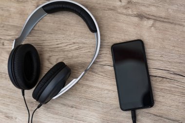 Siyah kulaklıklar ve ahşap masada akıllı telefon. Kulaklıklar ve ahşap masada fotokopi alanı olan akıllı telefon. Üst görünüm.