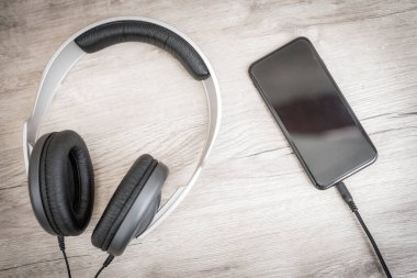 Siyah kulaklıklar ve ahşap masada akıllı telefon. Kulaklıklar ve ahşap masada fotokopi alanı olan akıllı telefon. Üst görünüm.