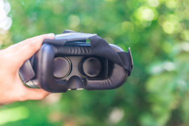 Sanal gerçeklik kulaklığı, Google. VR gözlükler, açık hava parkında çimlerin üzerinde oturan sanal gerçeklikle ekranı birbirine değdirin. VR kulaklık cihazı. Doğa arka planı. İnsanlar ve teknoloji kavramı