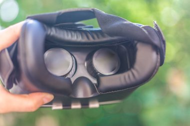 Sanal gerçeklik kulaklığı, Google. VR gözlükler, açık hava parkında çimlerin üzerinde oturan sanal gerçeklikle ekranı birbirine değdirin. VR kulaklık cihazı. Doğa arka planı. İnsanlar ve teknoloji kavramı