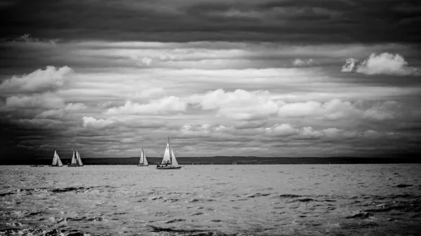 Sailboat at ocean horizon black and white, dramatic sky and clouds. Monochrome recreational sailing background with copy space for text