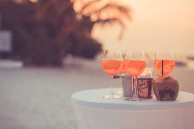 Plaj partisinde aperol spreyli kokteyller ve arka planda bulanık insanlar vardı. Sosyal etkinlik kaprisli afiş tasarımı sığ odak noktasında. Plaj partisinde bulanık insanlarla plaj günbatımı manzarası mum ışığında beyaz masadaki aperol içeceklerine odaklan