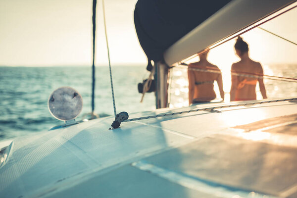 Silhouette of female friends relaxing on the yacht with during sunset on the high seas. 