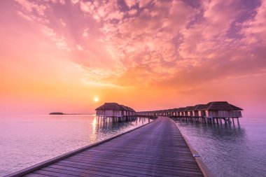 İnanılmaz günbatımı gökyüzü ve sakin deniz yansıması, Maldivler 'in su bungalovları üzerindeki lüks plaj manzarası. Yaz tatilinin egzotik manzarası ve tatil geçmişi. Maldivler adasında gün batımı, lüks su villaları tatil köyü ve ahşap iskele.