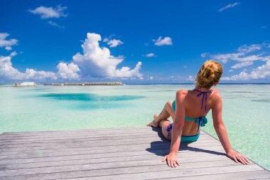 Genç moda kadını plajda dinleniyor. Rahatlatıcı ada yaşam tarzı. Tahta güverte, mavi gökyüzü ve kristal tropik plaj denizi ve su villaları. Cennet 'te tatil. Okyanus kumsalı dinlenme, Maldivler adalarına seyahat, plaj tatilcisi kadın.