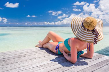 Egzotik deniz yolculuğu tatili. Lüks deniz manzarasına bakan bir kadın. yaz tatillerinde bikini ve hasır şapka giyerek lüks bir hayat süren çekici genç bir kadın. Ahşap güverteden deniz ve gökyüzü muhteşem görünüyor.