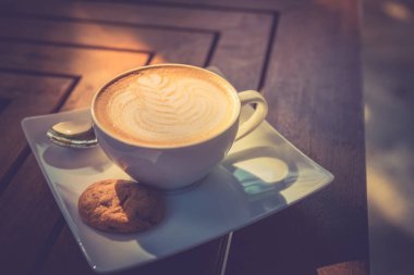 Sabah güneşi kahveli sütlü kahve sanatı. Latte sanat ve kurabiyeli beyaz kupa. Sabah havası, titreşimler, tatlı kapuçino.