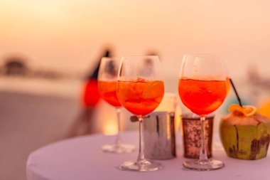 Aperol spreyli kokteyl içeceği, seçici odaklanma ve detaylar. Tropik plajda alkollü içecek. Plaj partisinde aperol spreyli kokteyller ve arka planda bulanık insanlar vardı. Sığ odak içinde sosyal etkinlik karamsar afiş tasarımı