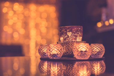 Masa yansımalı güzel mum ışığı ve arka planda altın renkli bulanık ışık. Noel tatili konforlu ev içi yakın çekim. Romantik cam kavanozlar ve yanan mumlar.
