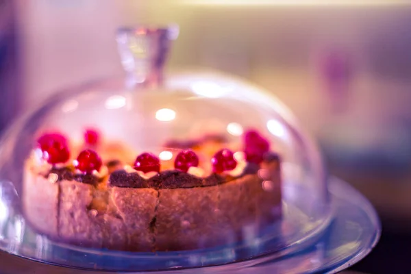 Fruit cake under glass bell dome. Cake stand, dessert buffet, storage, blurred sweatshop background