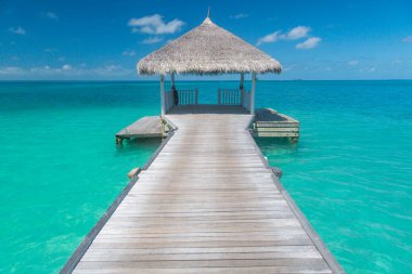 Muhteşem güneşli mavi körfez manzarası, mavi gökyüzü ve ahşap iskeleli bulutlar ve su evi üzerinde sonsuz ufuk. Meditasyon gevşemesi tropikal arka plan, deniz suyu. Gökyüzü deniz manzarası arka planı. Huzur egzotik cennet, inanılmaz seyahat konsepti.