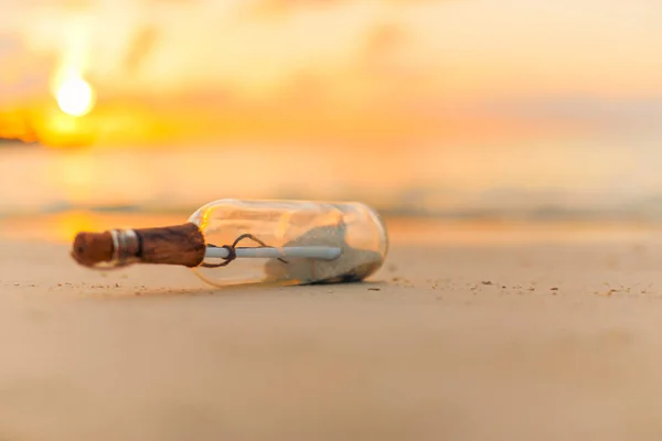 Message in the bottle washed ashore against the sun setting down. Tropical beach design background, message in a bottle on a sea shore
