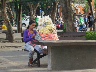 Denpasar, Endonezya - 28 Eylül 2019: Puputan Badung Meydanı 'ndaki park bankında oturmuş abur cubur ve meyve dilimi satan bir sokak satıcısı.