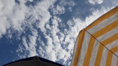 Bir şeritli plaj şemsiyesi ile bulutlu ve güneşli gökyüzü