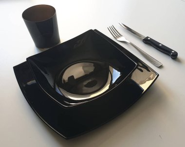 Siyah tabak, gümüş çatal ve siyah bıçaktan oluşan siyah masa seti beyaz masada.