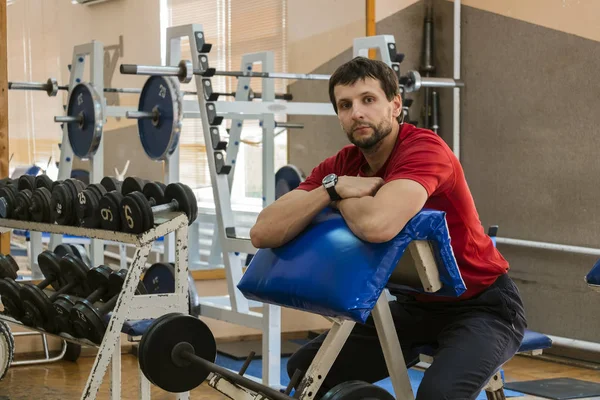 Basit bir küçük spor salonunda genç eğitmeni Scott tezgah oturur
