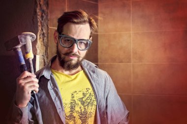 Koruyucu gözlük sakallı usta bir balyoz ve bir keski elinde tutuyor