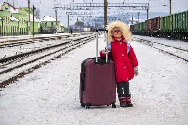 Büyük bir çanta ile kız bebek tren istasyonu boş karla kaplı platformu üzerinde duruyor ve gökyüzüne görünüyor