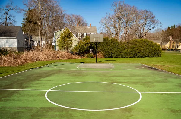 green recreational basketball court in a park with houses in background, United States