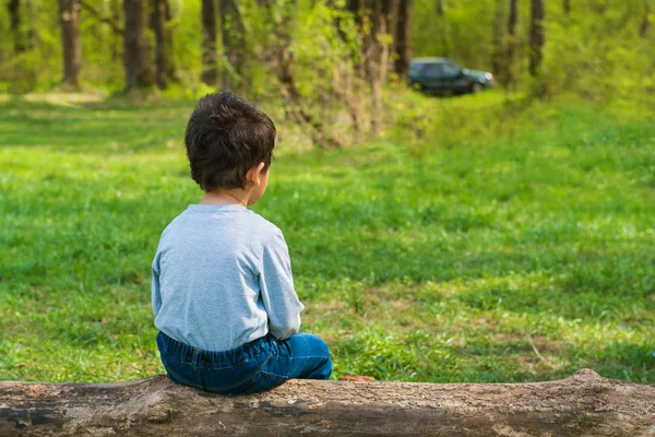 dark-haired boy sitting on a log alone