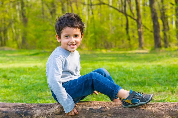 Braunäugiger Junge Sitzt Auf Einem Baumstamm Und Lächelt — Stockfoto