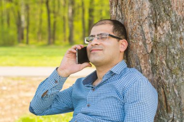 adam parkta bir ağacın altında bir akıllı telefon ile