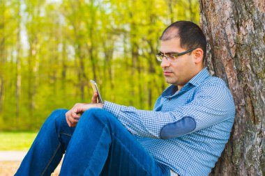 adam parkta bir ağacın altında bir akıllı telefon ile