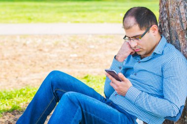 adam parkta bir ağacın altında bir akıllı telefon ile