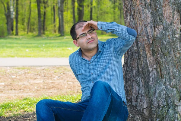 man sits under a tree and looks into the distance