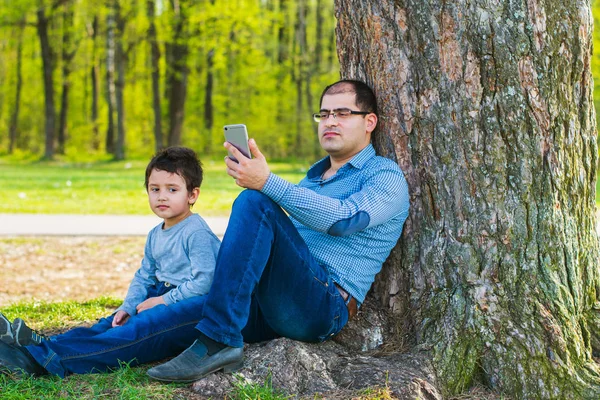 Padre Hijo Sentados Bajo Árbol Verano Papá Está Ocupado Con — Foto de Stock