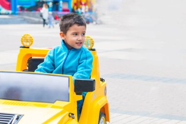 esmer çocuk parkta bir elektrikli sarı araba sürmek