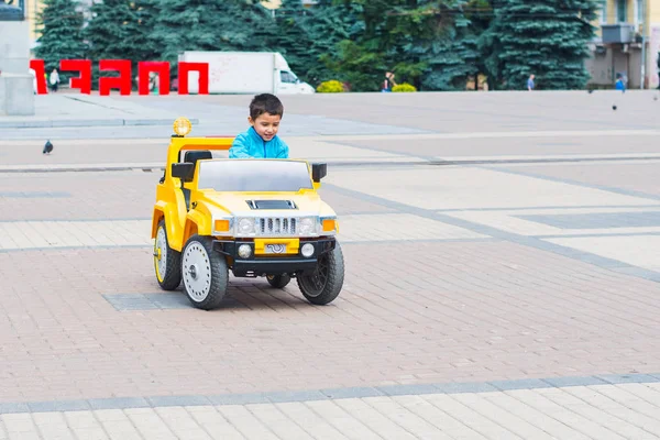 Brunette Boy Rides Electric Yellow Car Park — Stock Photo, Image