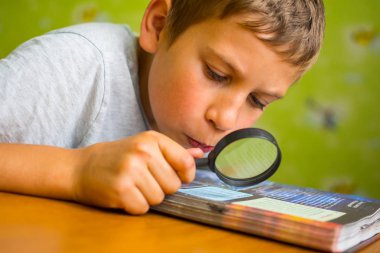 sarışın çocuk heyecanla bir büyüteç ile bir kitap okuma