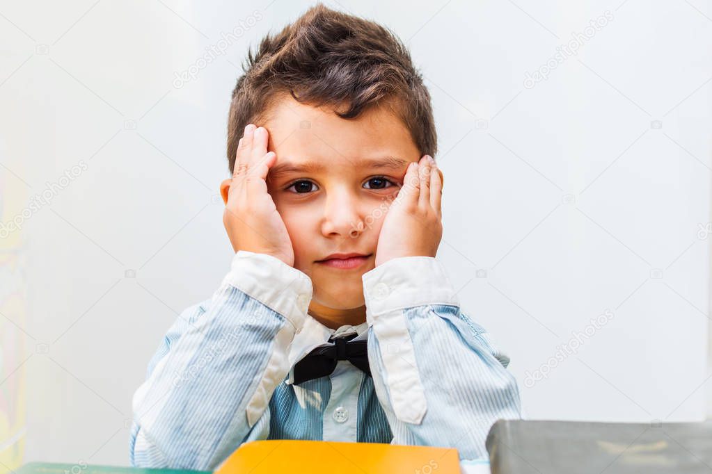 boy at the table with the books holding his face