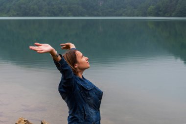 Göl arka plan üzerinde yükseltilmiş kolları olan genç kadın