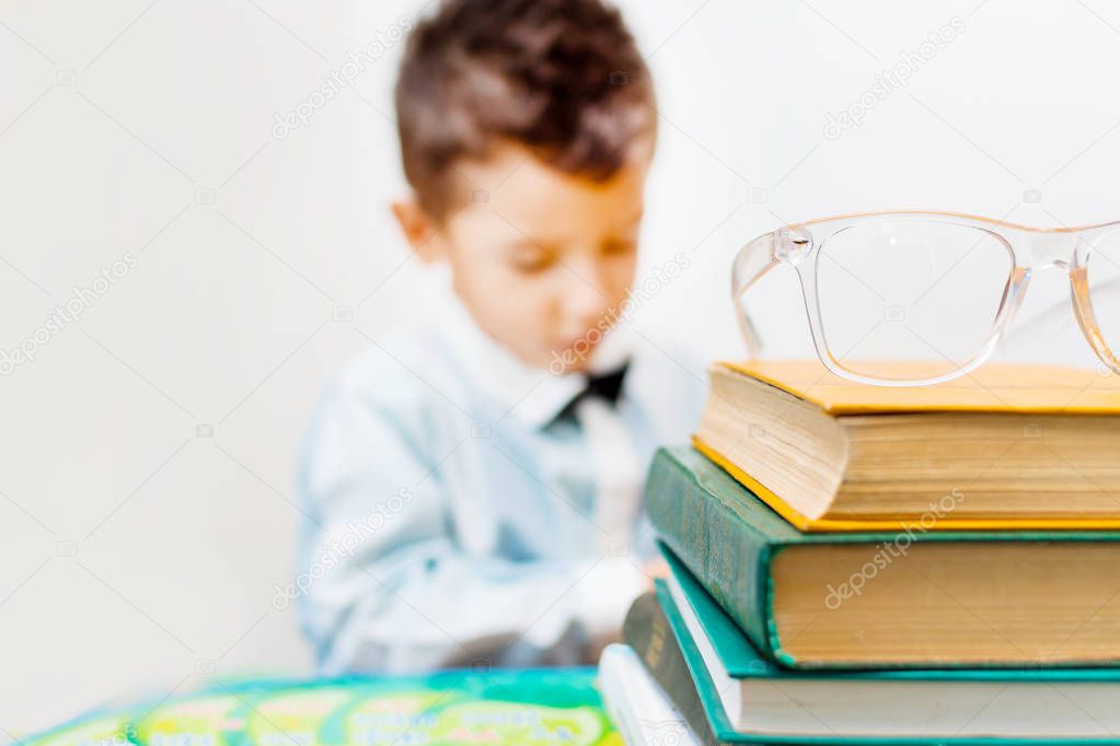 glasses on a stack of books, boy in the background blurred.