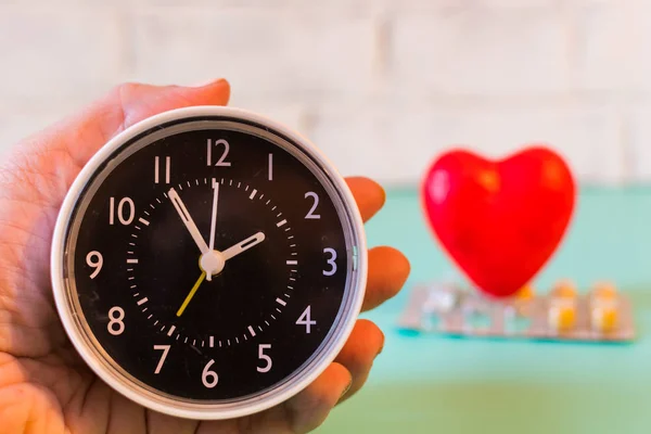 clock in hand on the background of blister of tablets and heart