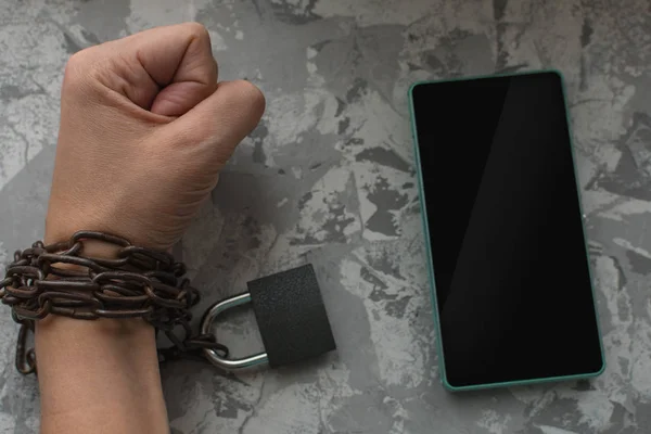 Hand wrapped in a chain and next to the smartphone. the concept — Stock Photo, Image