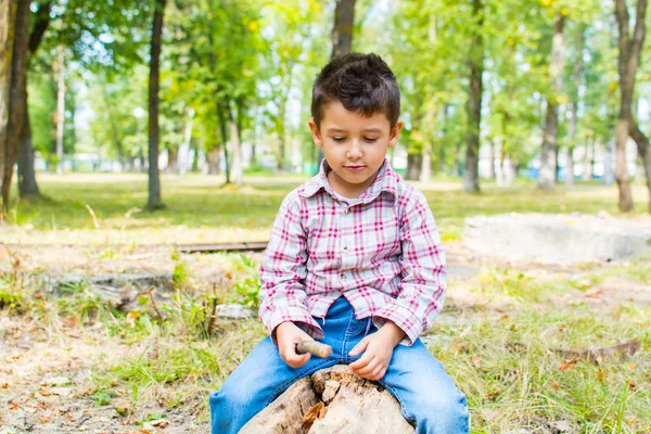 Мальчик в парке, сидящий на бревне — стоковое фото