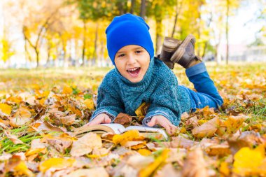bir kitap ile sarı yaprakları üzerinde yatan neşeli çocuk