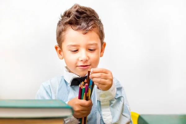 Brown-Eyed Boy i en skjorta med blyertspennor omgiven av böcker — Stockfoto