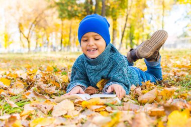 bir kitap ile sarı yaprakları üzerinde yatan neşeli çocuk
