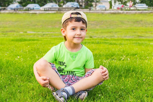 Happy boy sitting on the grass in the summer — Stock Photo, Image