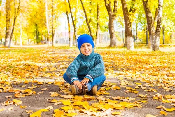 Улыбающийся мальчик в шляпе и свитере, сидящий в парке на ауту — стоковое фото